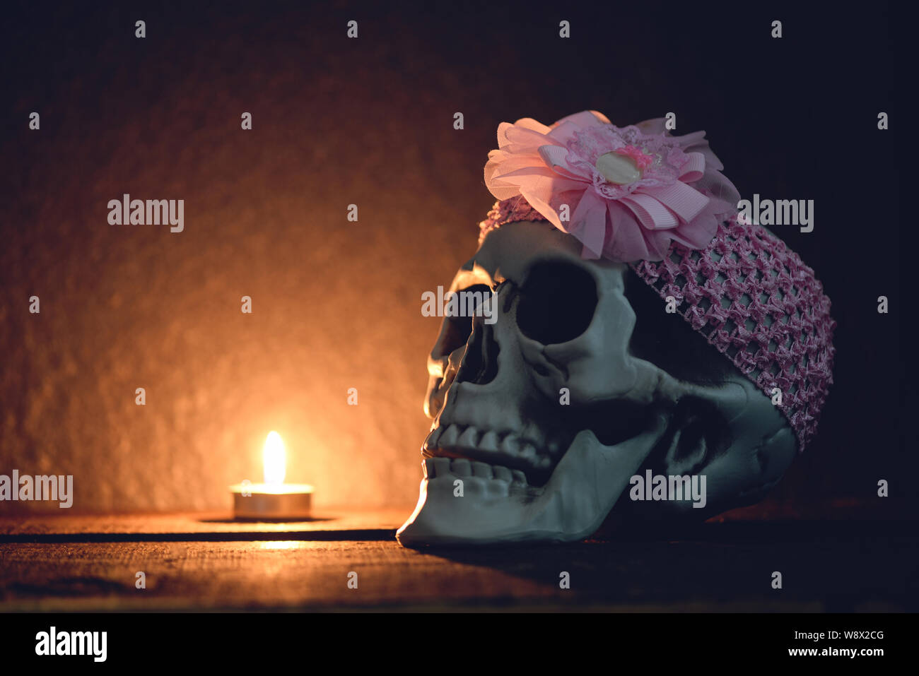 Cranio still life / teschio umano con archetto rosa intorno decorata a festa di Halloween e la luce candela su sfondo scuro Foto Stock