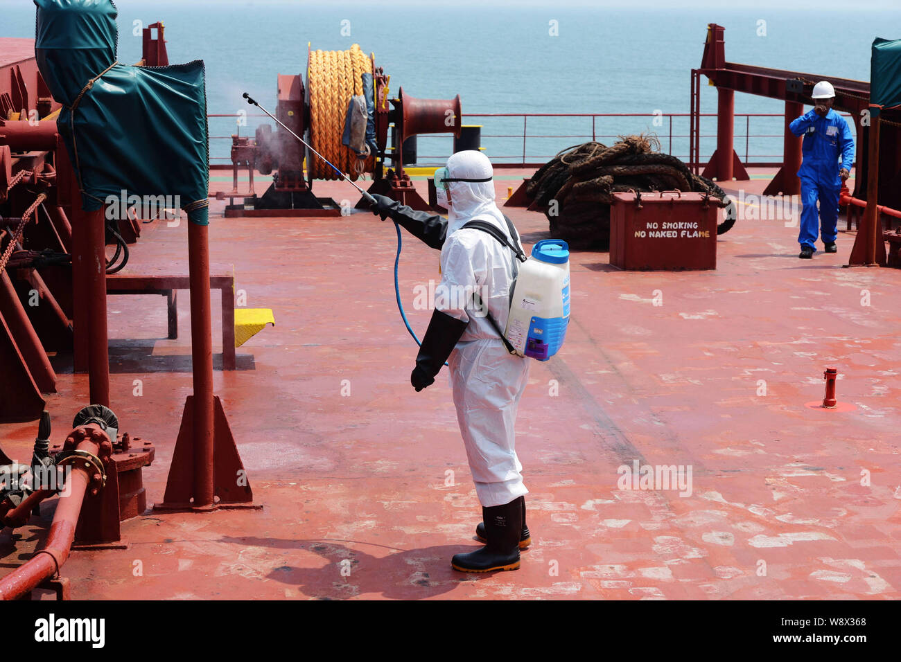Una quarantena cinese lavoratore indossando indumenti protettivi disinfetta il ponte della nave che trasporta merci alla rinfusa alfa amicizia il trasporto di minerali da Ebola-colpite si Foto Stock