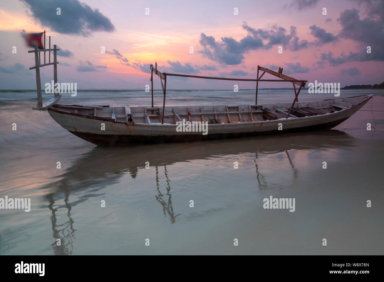 Una lunga esposizione di una barca da pesca su Otres spiaggia al tramonto con movimento sfocate (onde e bandiera cambogiana), Sihanoukville, Cambogia. Foto Stock