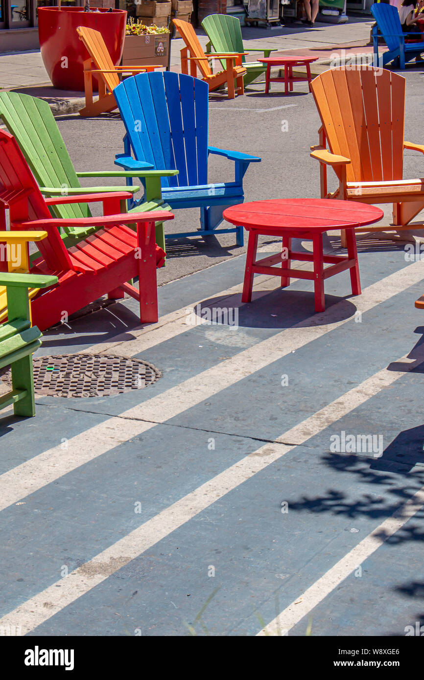 Vivacemente colorate sedie in legno circondano le tavole rotonde su una strada in un centro di mercato su una giornata di sole. Foto Stock