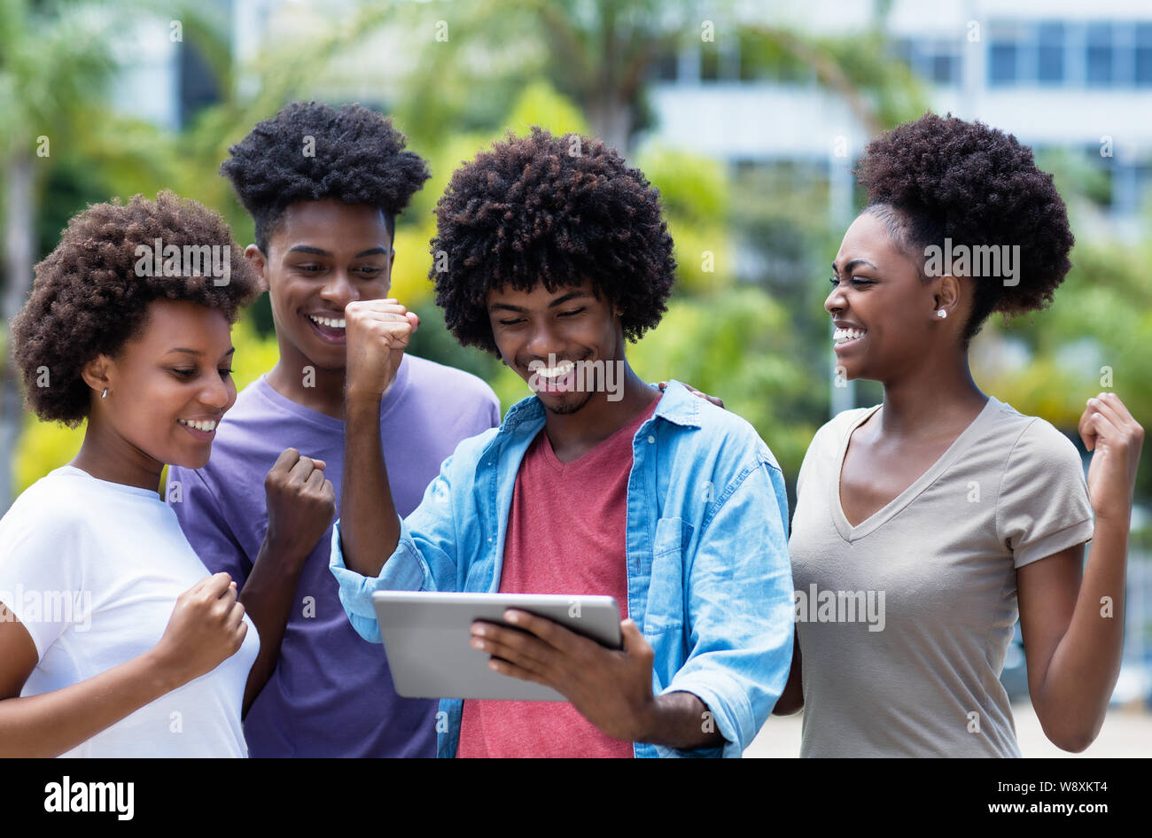 Il tifo del gruppo americano africano degli studenti universitari con tavoletta digitale all'aperto in estate Foto Stock