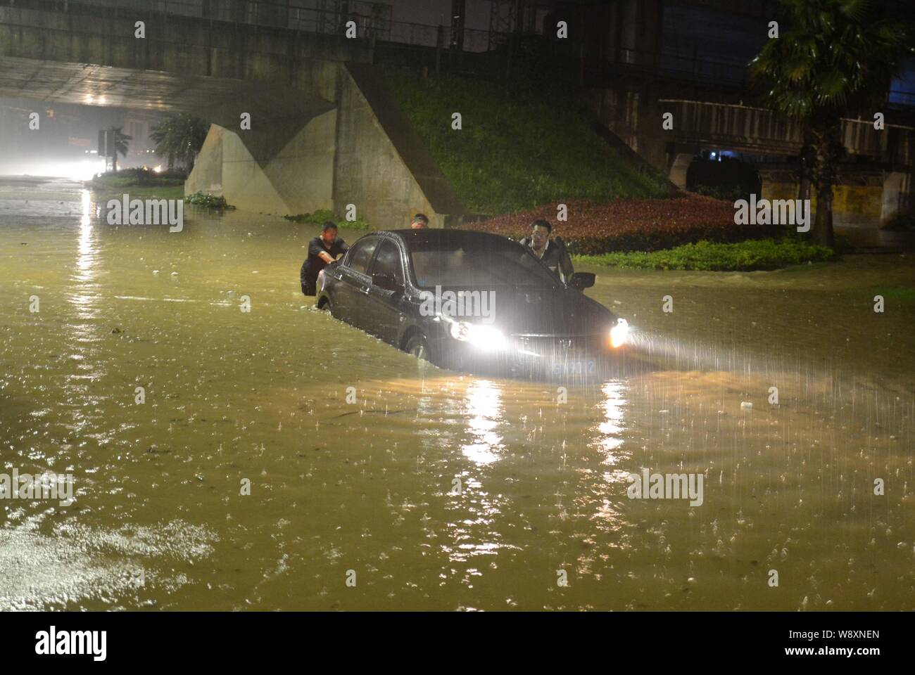 I residenti locali spingere le loro auto in un invaso street causato da un pesante acquazzone in lo sviluppo economico e tecnologico in zona Città Jiujiang, ea Foto Stock