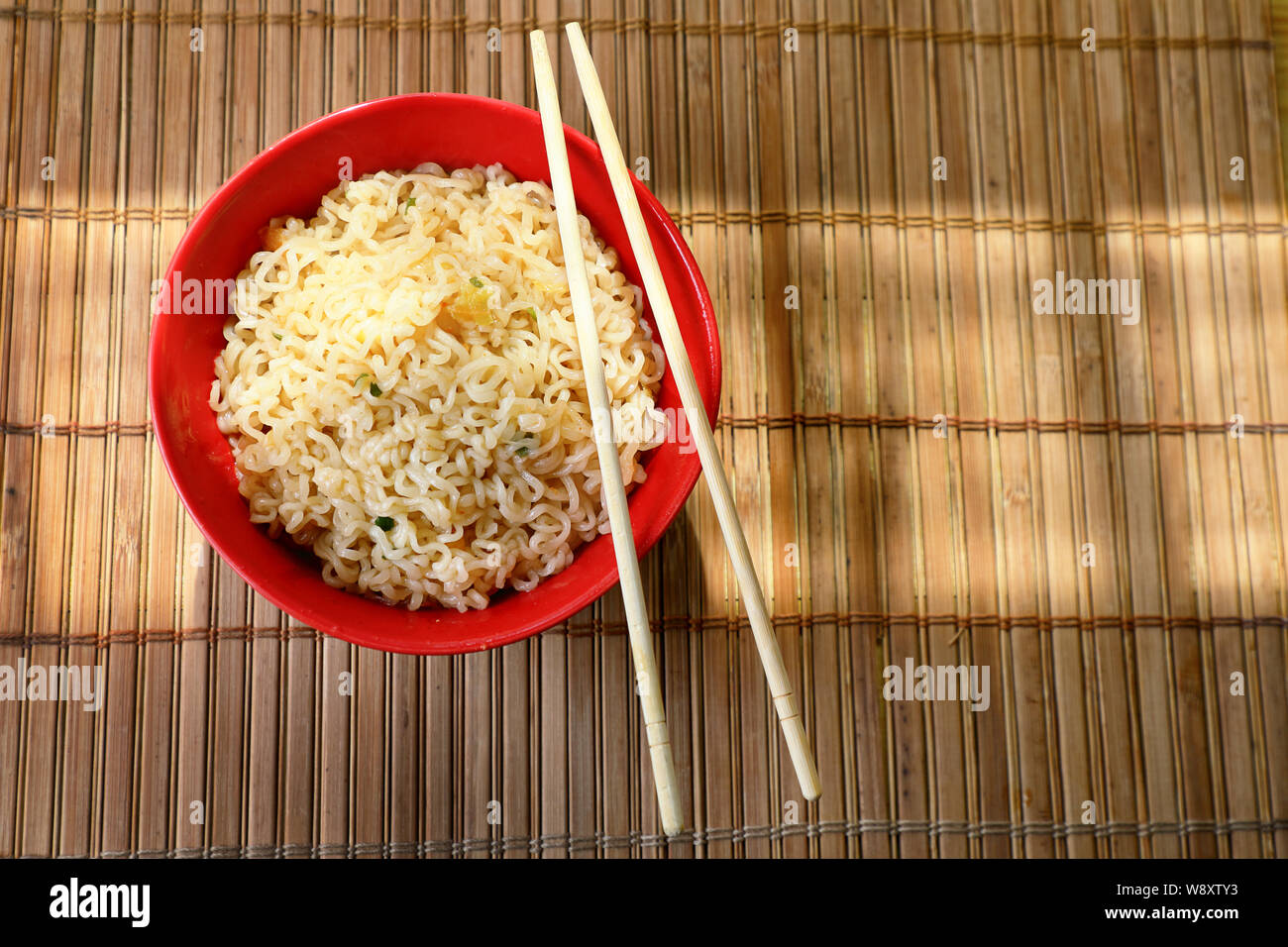 Stile asiatico tagliatelle in un bicchiere di rosso con bacchette. contro un tappetino di bambù . Foto Stock