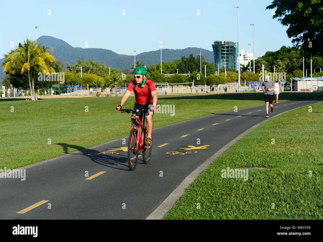 Ciclista maschio in una camicia rossa a cavallo su una corsia di ciclismo in Cairns, estremo Nord Queensland, FNQ, QLD, Australia Foto Stock