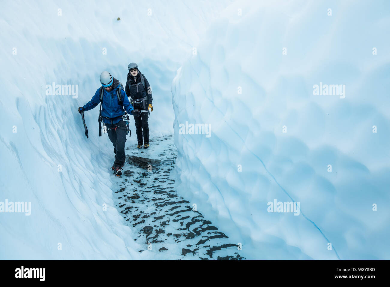 Giovane uomo e donna a piedi attraverso un canyon del ghiacciaio sul ghiacciaio Matanuska. Nel fondo del canyon è chiara, acqua fredda abbastanza profondo per Foto Stock