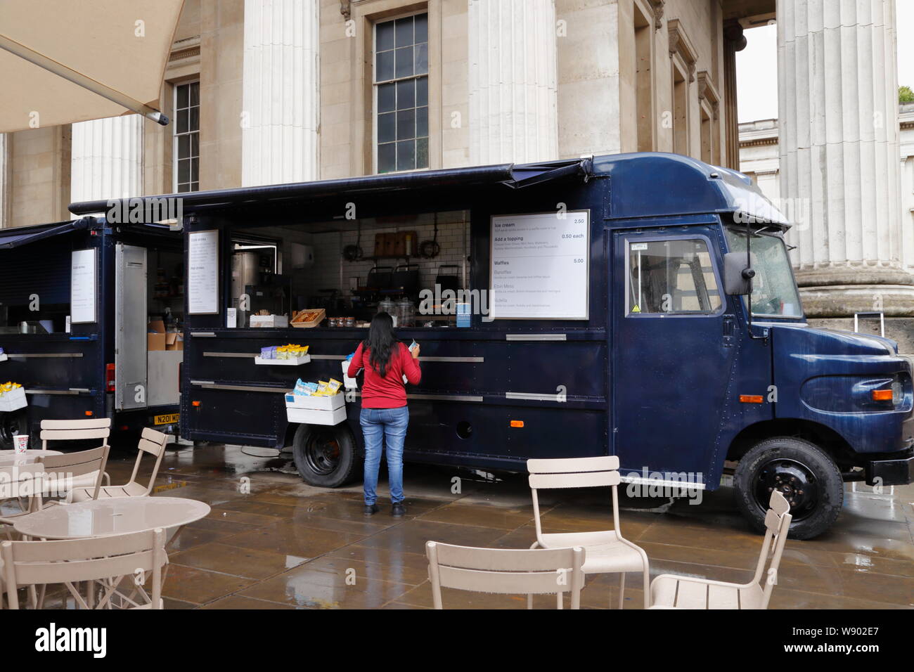 Una donna acquista rinfreschi da un camion di cibo nel cortile del British Museum di Londra, Regno Unito, in una piovosa giornata estiva. Foto Stock