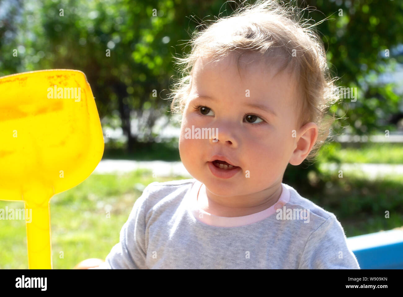 Ritratto di un po' di baby boy girl close-up. Il capretto con un giallo pala in plastica per una passeggiata nella natura bambino bambino in un maglione grigio passeggiate nel parco giochi Foto Stock