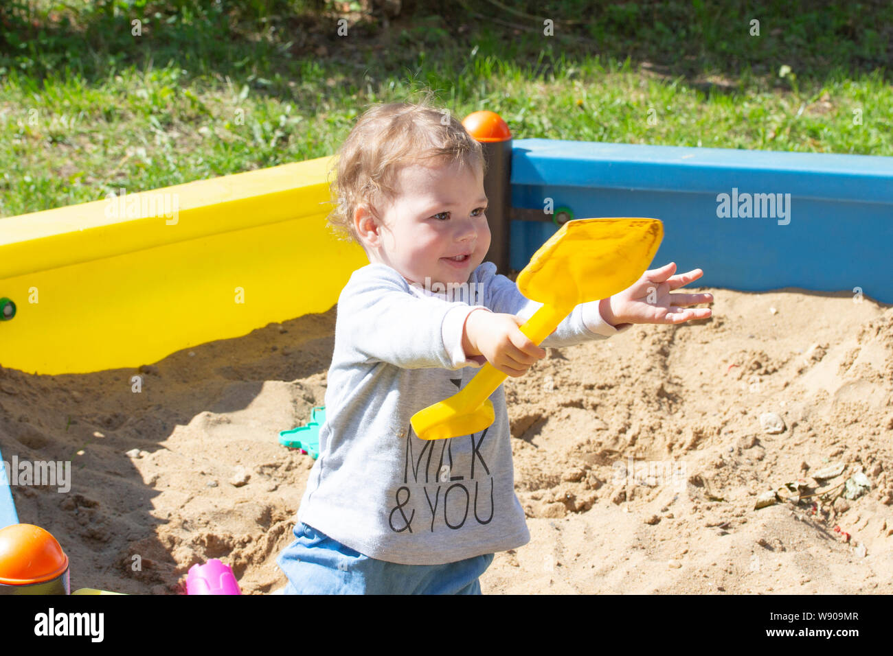 Allegro bambina ragazzo giocando con una pala nel sandbox. Ridere faccia sorridente bambino bambino in un maglione grigio passeggiate nel parco giochi, giocando con s Foto Stock
