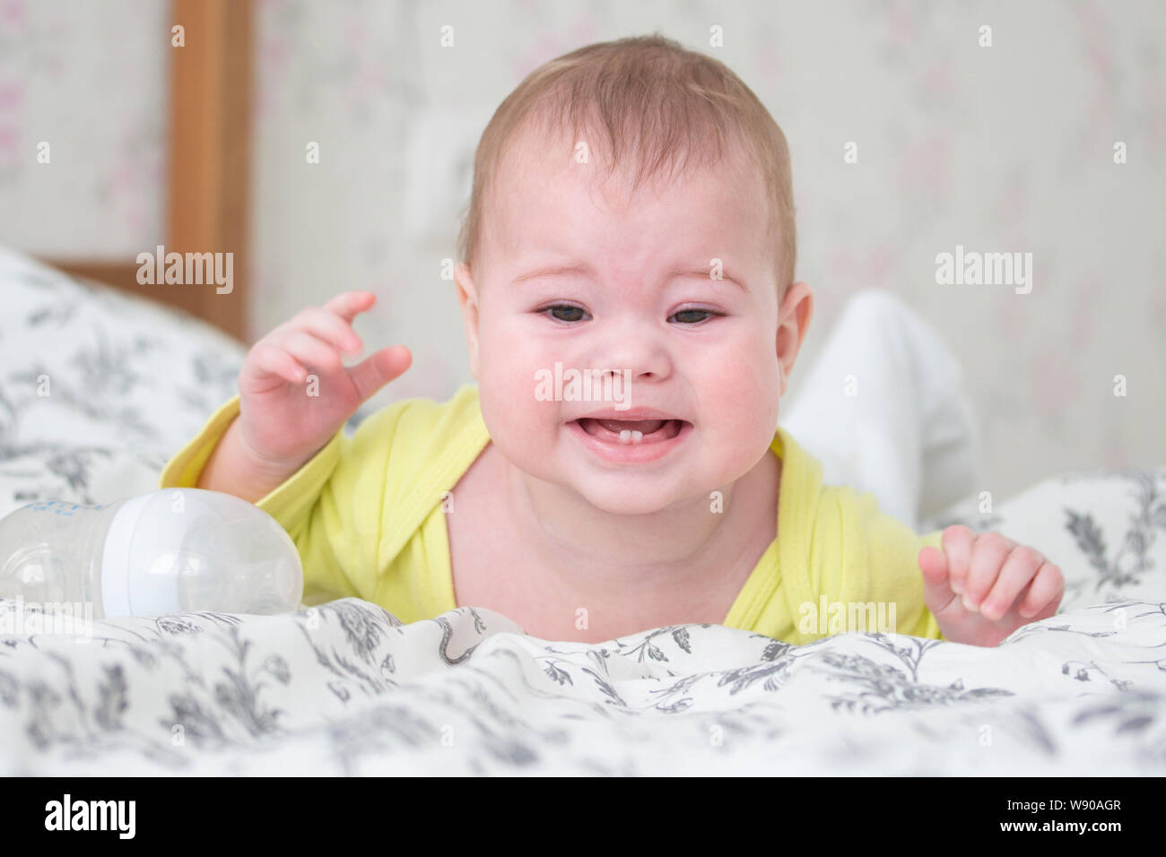 Baby 6-7 mesi a piangere giacente sul suo stomaco. caucasica ragazza ragazzo bambino kid bimbo neonato in giallo grida e mostra 2 denti baby, dentizione, ritratto così Foto Stock