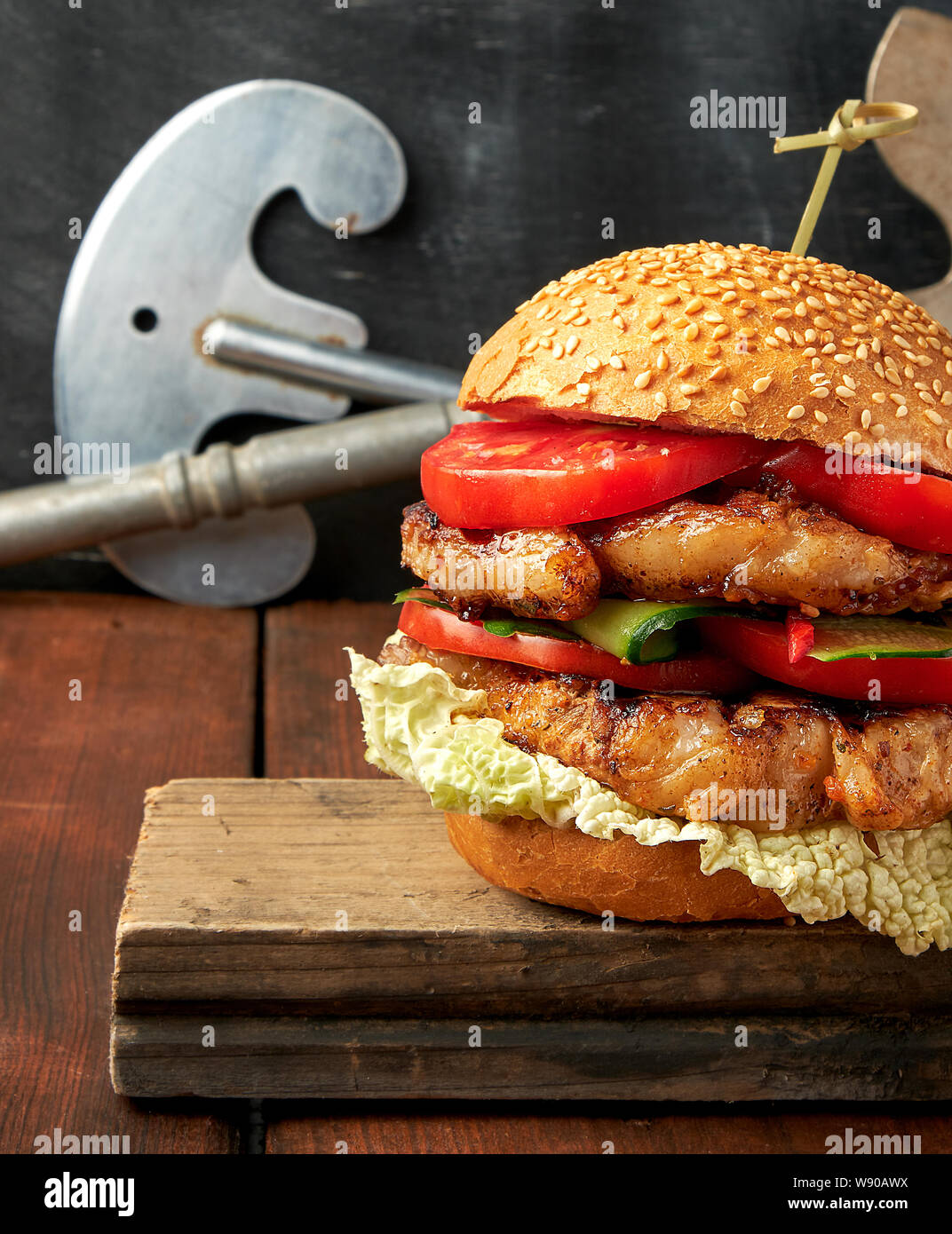 In casa il doppio hamburger con carne di maiale fritto bistecca, pomodori rossi freschi round bun con semi di sesamo su un vintage tavola di legno Foto Stock