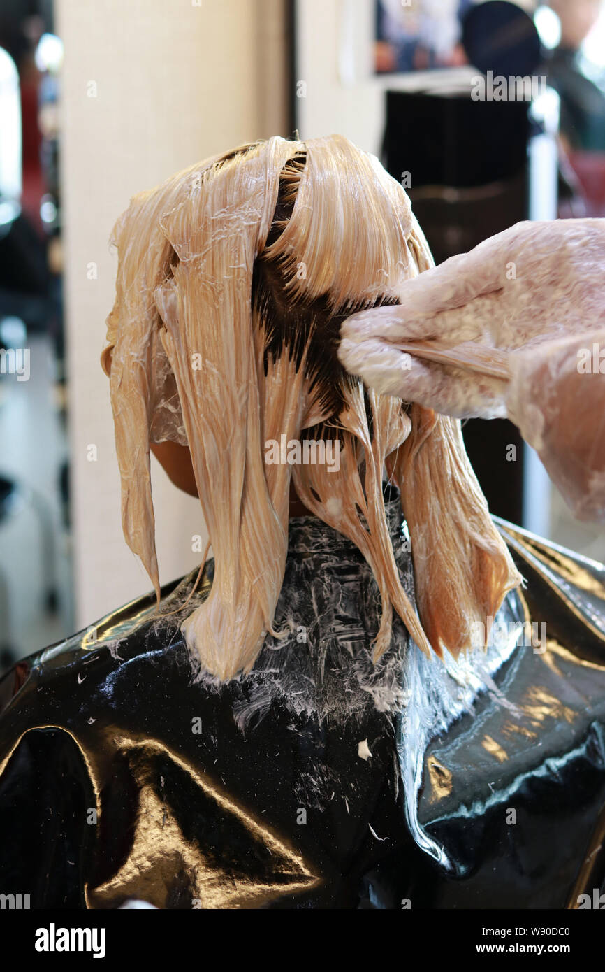 Parrucchiere mano tirando alcuni capelli e applicare colore crema schiarente in salone Foto Stock