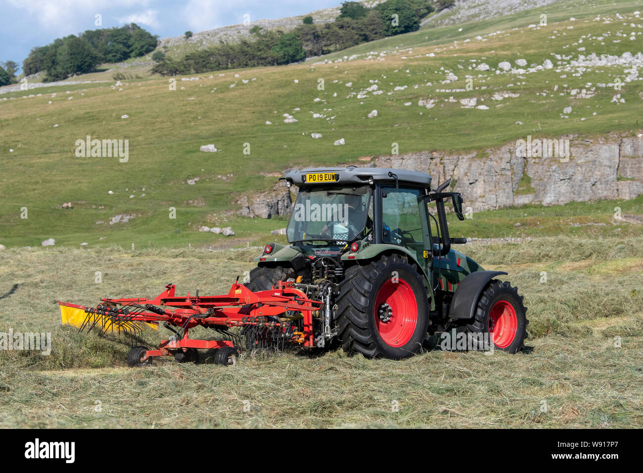 Agricoltore remare fino al fieno con un trattore Hurlimann e a due pass rastrello su una collina di pennini agriturismo vicino a Ravenstondeale, Cumbria. Foto Stock
