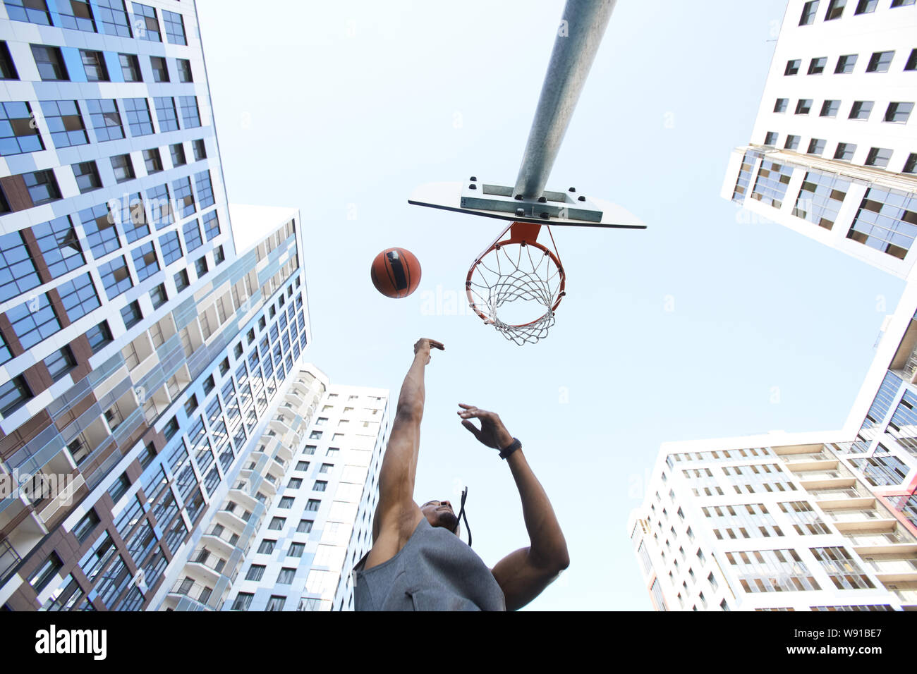 Basso angolo di visione a pallacanestro africana di tiro del giocatore Slam Dunk contro sky in background urbano, spazio di copia Foto Stock