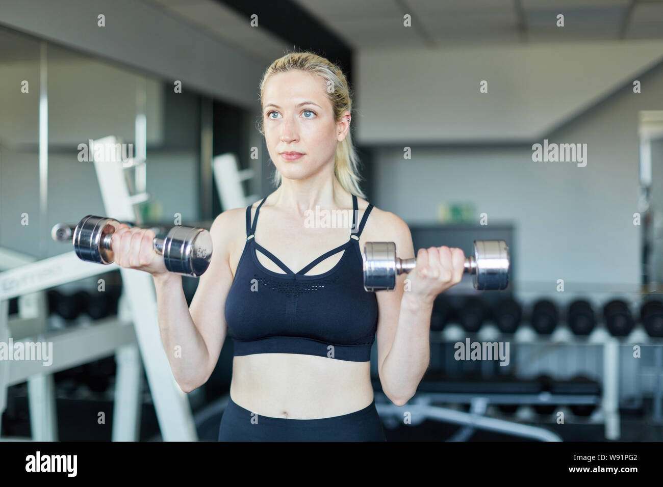 Giovane donna treni forza e muscolo bicipite con manubri in centro fitness Foto Stock