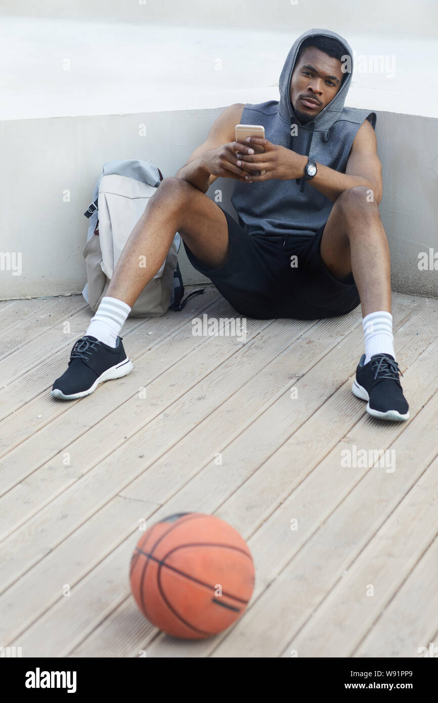A piena lunghezza Ritratto di bello afro-americano di uomo utilizza lo smartphone durante i momenti di relax nel parco all'aperto, spazio di copia Foto Stock
