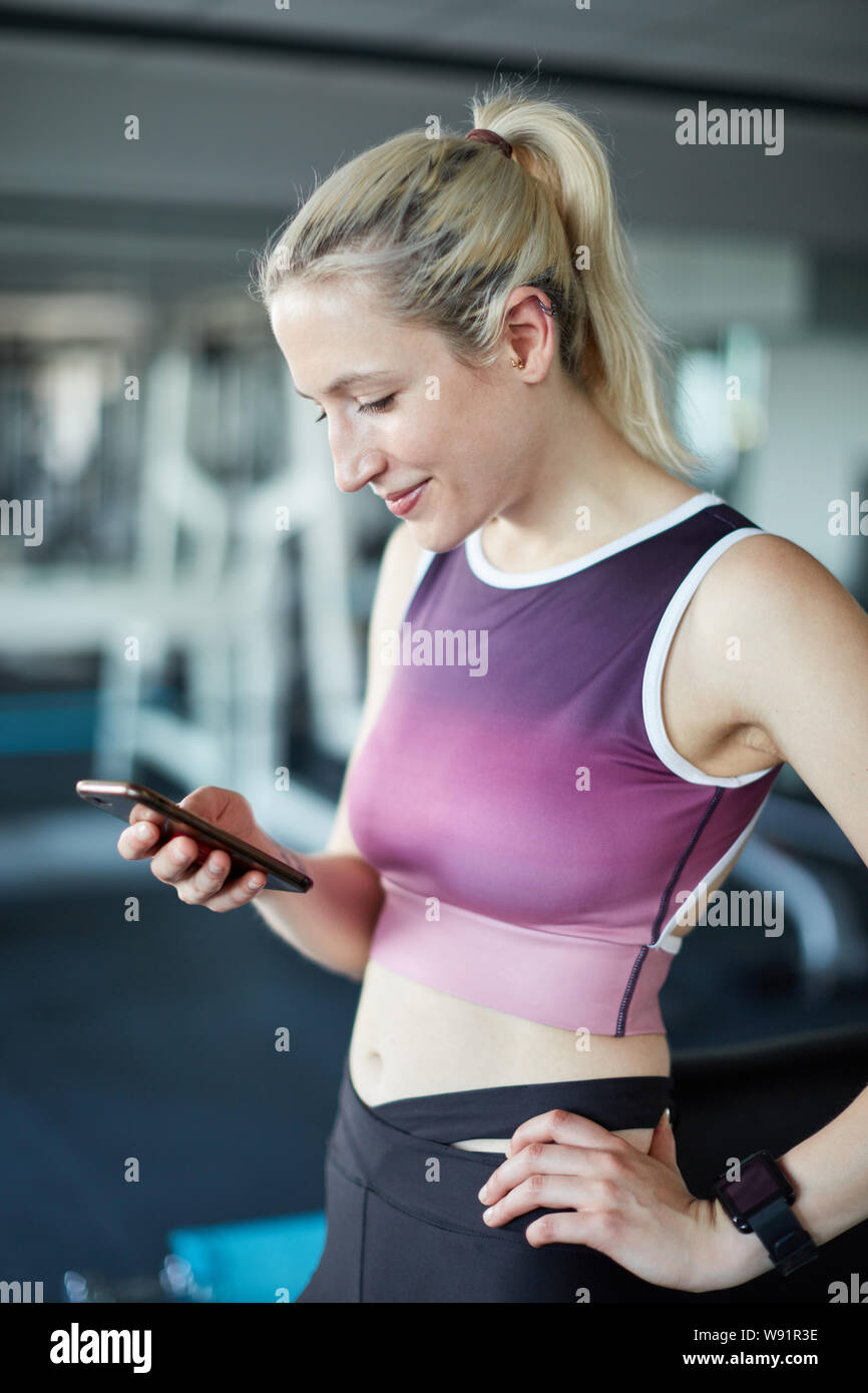 Giovane donna attentamente legge un messaggio di testo sullo smartphone nel centro fitness Foto Stock