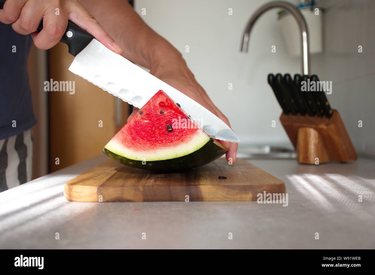 Primo piano della donna di mano anguria di taglio sul tagliere di legno in cucina Foto Stock