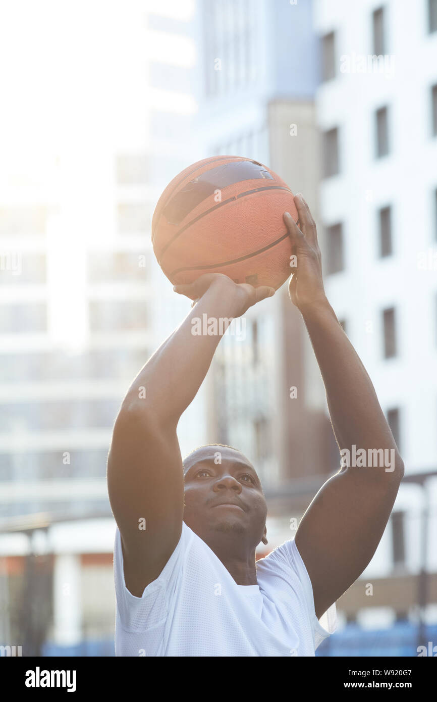 Alta sezione ritratto di muscolare uomo africano gettando il basket ball all'aperto, spazio di copia Foto Stock
