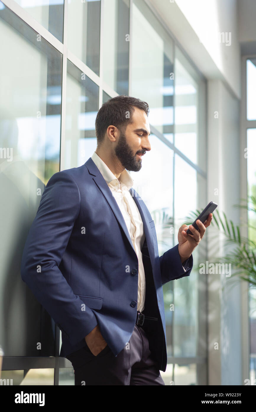 Felice barbuto imprenditore appoggiata sulla parete di vetro Foto Stock