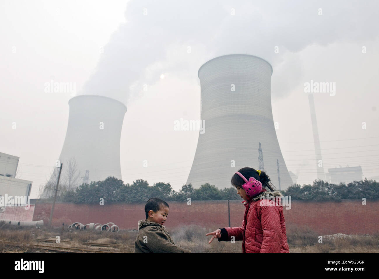 Due giovani bambini giocano il finger-gioco degli indovinelli vicino a torri di raffreddamento e i camini di fumo discharing presso un impianto alimentato a carbone in pesanti smog in Luoyang ci Foto Stock