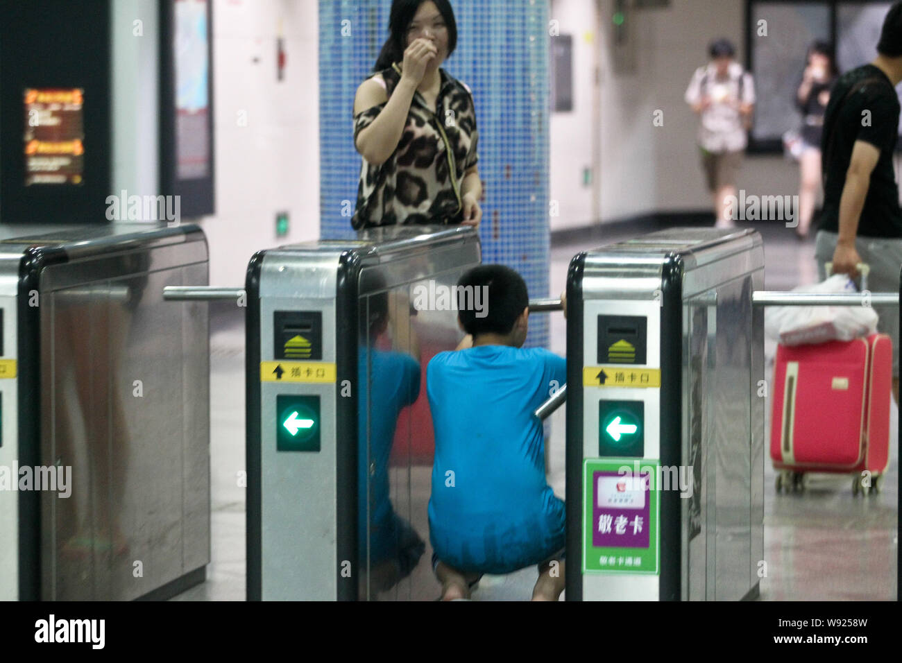 Un passeggero cinese worm il suo modo attraverso un tornello a Xizang Road S. La stazione della metropolitana di Shanghai, Cina, 12 agosto 2013. La metro di Shanghai sai Foto Stock