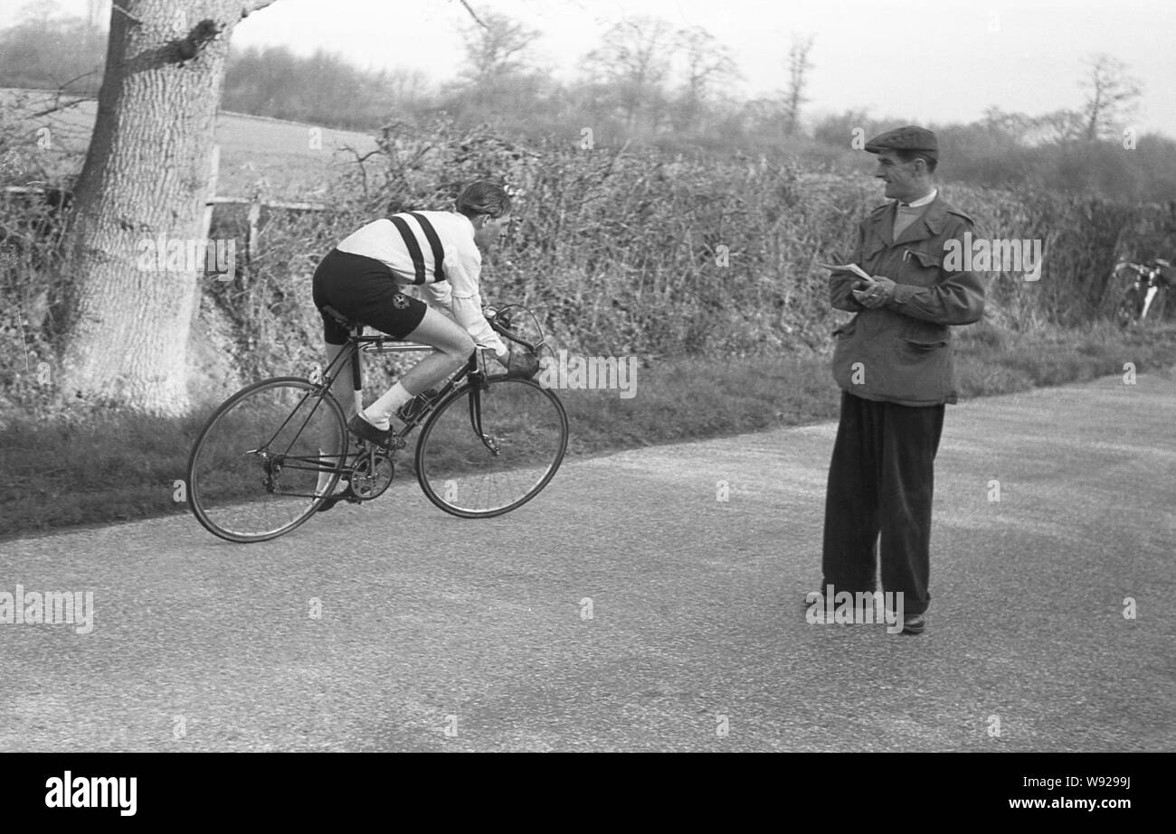 Degli anni Cinquanta, storico dilettante tempo maschio-ciclista prova andando attorno a un ufficiale su una strada, circa per girare e la testa indietro lungo il percorso che ha appena venuti da, Inghilterra, Regno Unito. Foto Stock