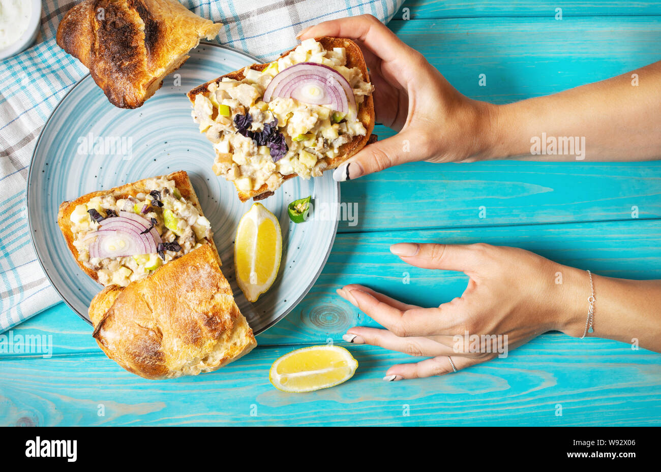 Mani femminili tenere macinate di Filetto di aringa con Apple e uovo su tostati Pane di segale, in casa di tradizionale cucina ebraica piatto forshmak blu sulla tavola di legno. Foto Stock