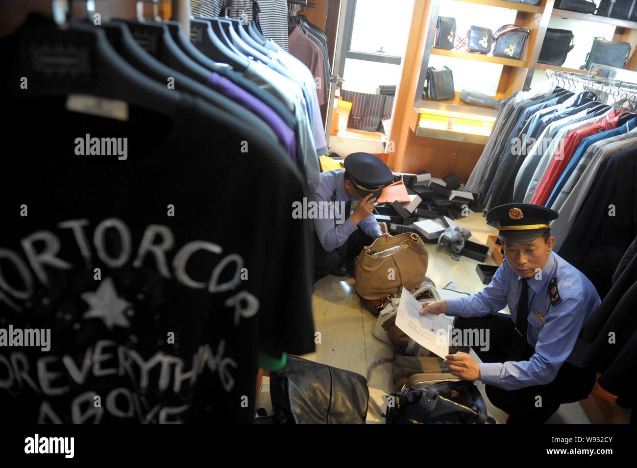 La legge cinese i funzionari di polizia confiscare fake brand di lusso magliette e borsette in un negozio a Pechino, in Cina, il 13 maggio 2013. La polizia di Pechino e l Foto Stock