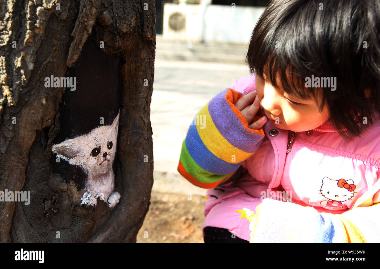 --FILE -- una bambina guarda un bat-eared Fox dipinta in un foro albero dai cinesi studente di college Wang Yue su di una strada nella città di Shijiazhuang, mento del nord Foto Stock