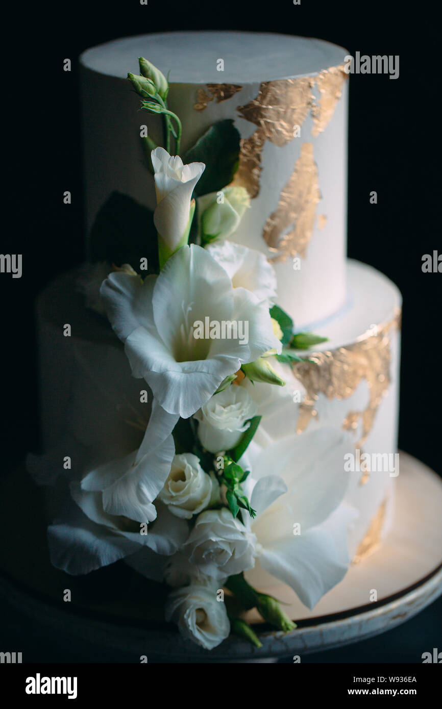 Due livelli di torta con fiori su un supporto di legno su uno sfondo nero. Foto Stock