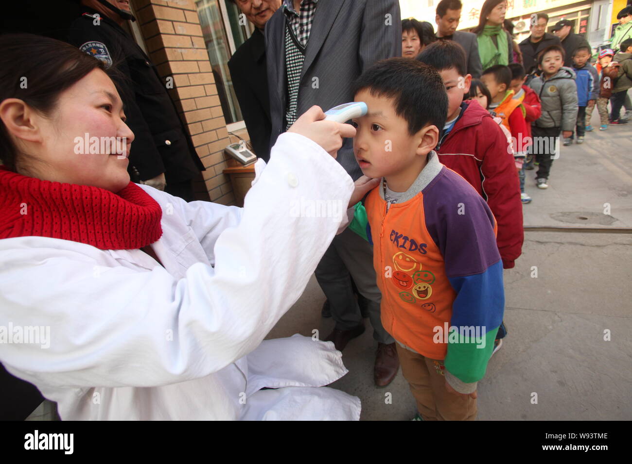 Un medico cinese lavoratore rileva la temperatura del corpo di giovani bambini fodera fino alla porta di un asilo nido nel corso di una campagna contro l'H7N9 av Foto Stock