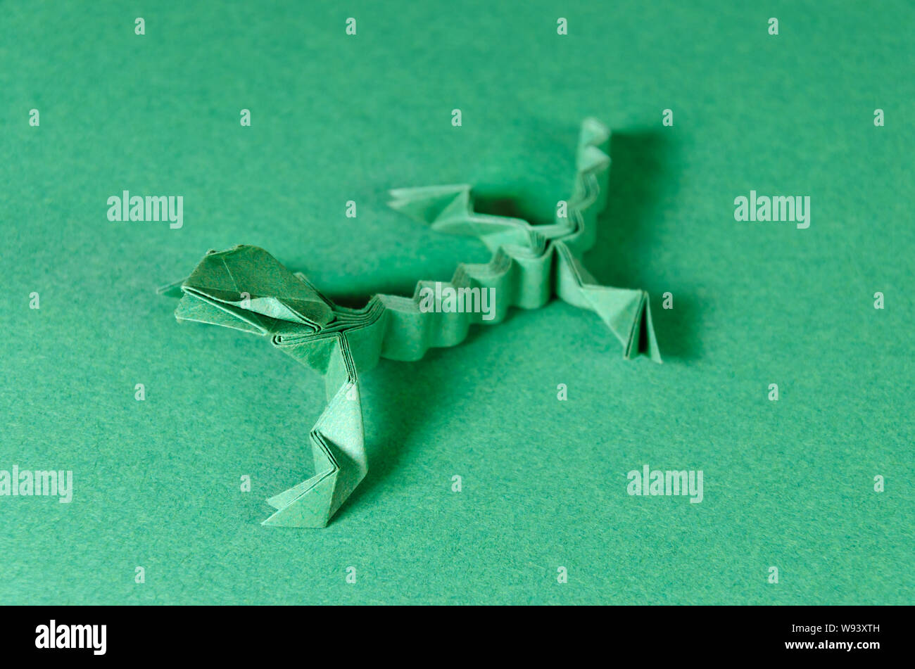 Verde lucertola origami su sfondo verde. Arte giapponese di piegatura della carta. Quadrato piatto foglio di carta trasferiti in una scultura finito. Foto Stock