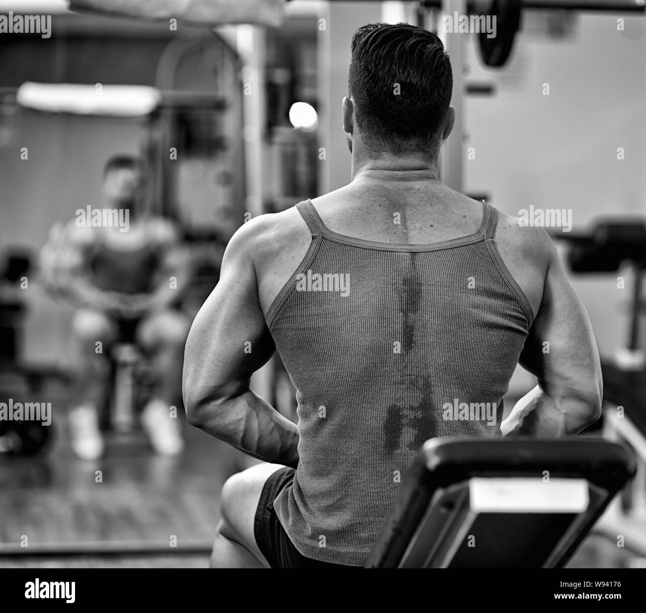 Forte uomo atletico in palestra guardando la sua immagine riflessa nello specchio e preparazione per allenamento Foto Stock
