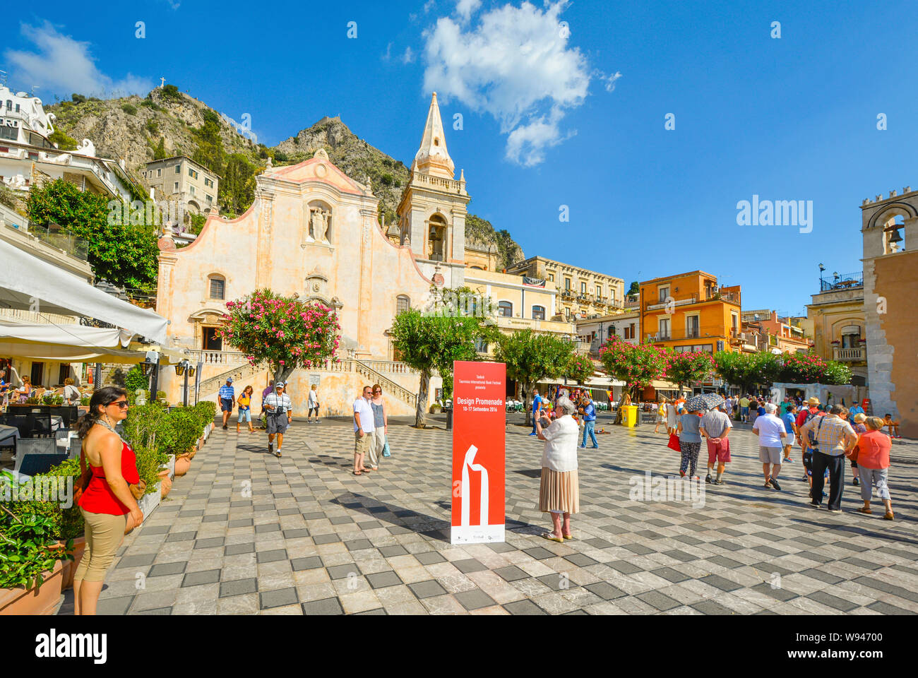 I turisti potranno godersi un pomeriggio estivo di fronte alla Chiesa di San Giuseppe, sulla trafficata Piazza Aprile a Taormina, sull'isola italiana della Sicilia. Foto Stock