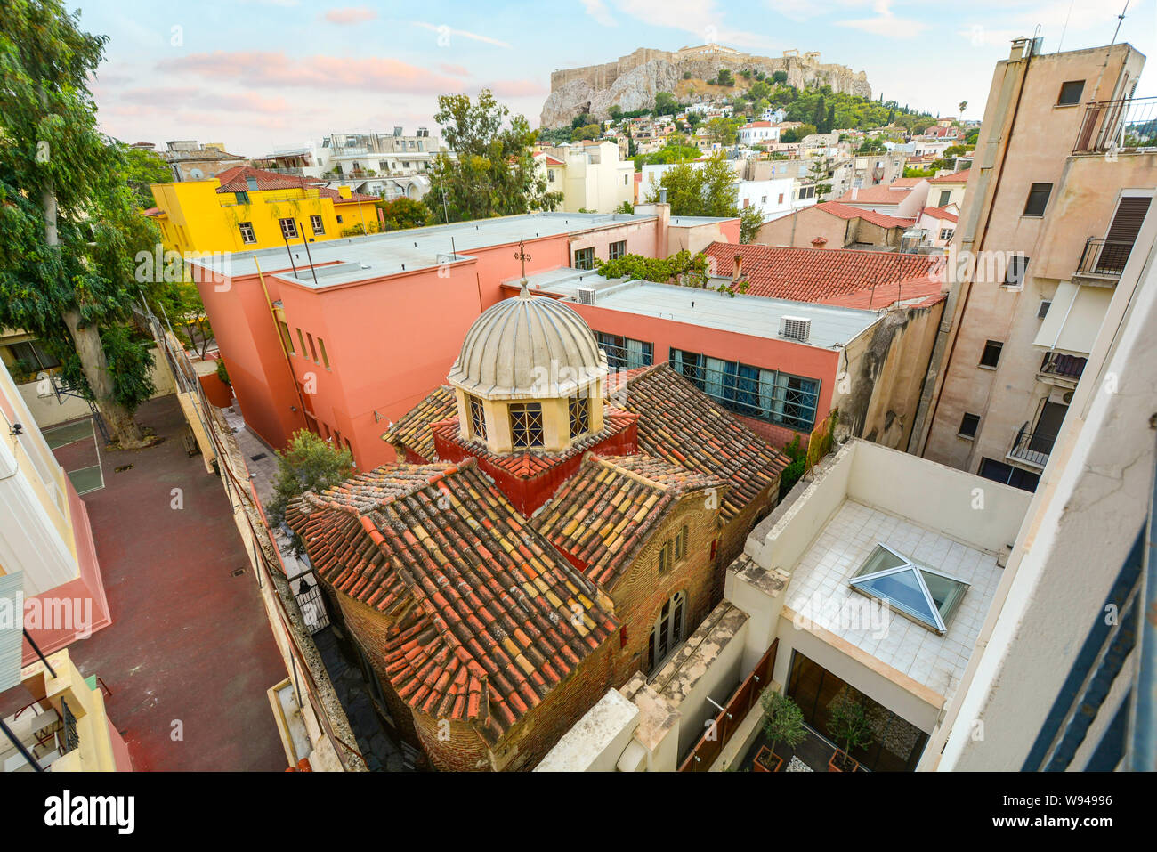 Un antica chiesa Greco Ortodossa è schiacciato tra più edifici moderni nel centro storico di Atene, Grecia, con Acropoli collina alle spalle. Foto Stock