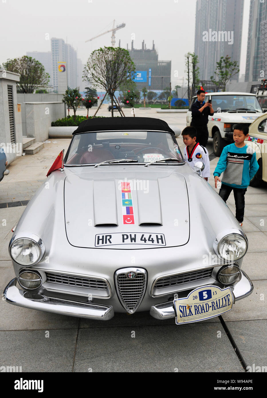 Giovani visitatori cinesi guardare una vecchia auto timer di Alfa Romeo che ha compiuto 2013 Silk Road Rallye durante una mostra a Quanshun shopping p Foto Stock