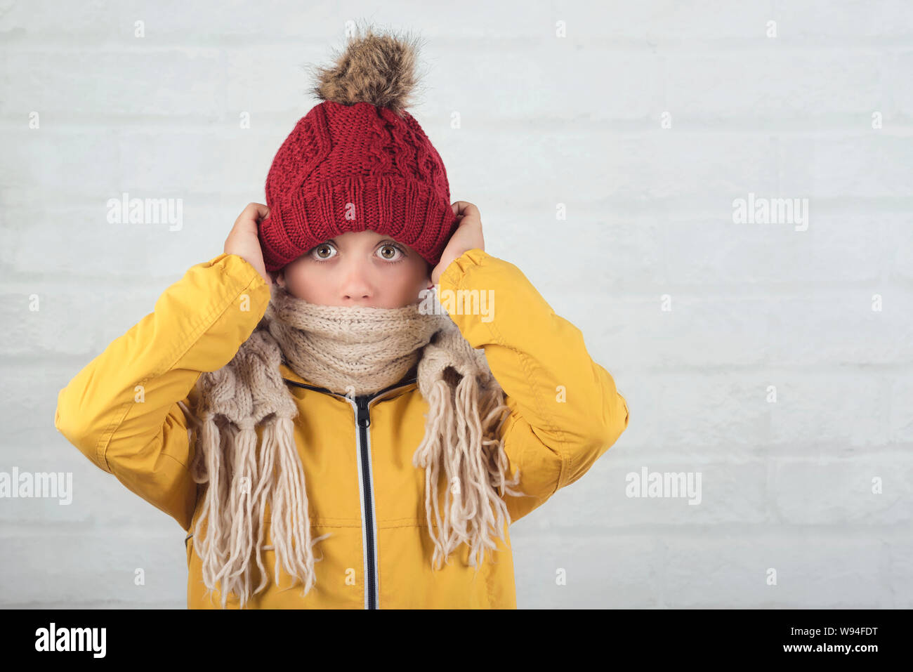 Funny bambino con cappello invernale e sciarpa contro Sfondo mattone Foto Stock