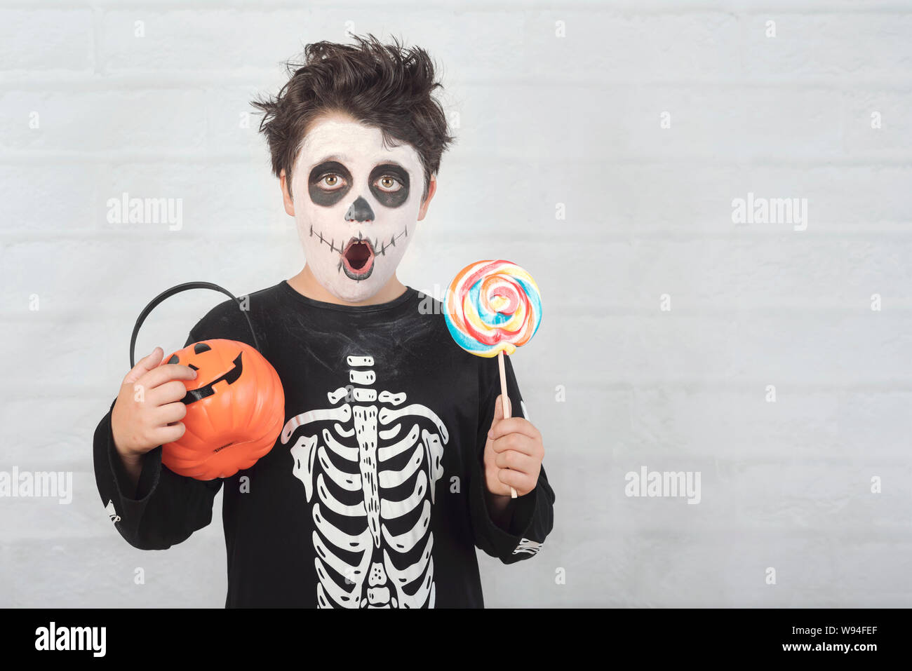 Happy Halloween.divertente bambino in un costume di scheletro di mangiare lecca-lecca di halloween contro Sfondo mattone Foto Stock