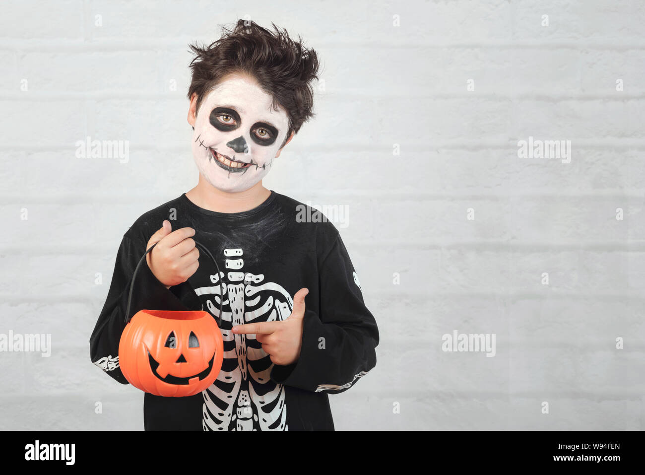 Happy Halloween.divertente bambino in un costume di scheletro con zucca di Halloween contro Sfondo mattone Foto Stock