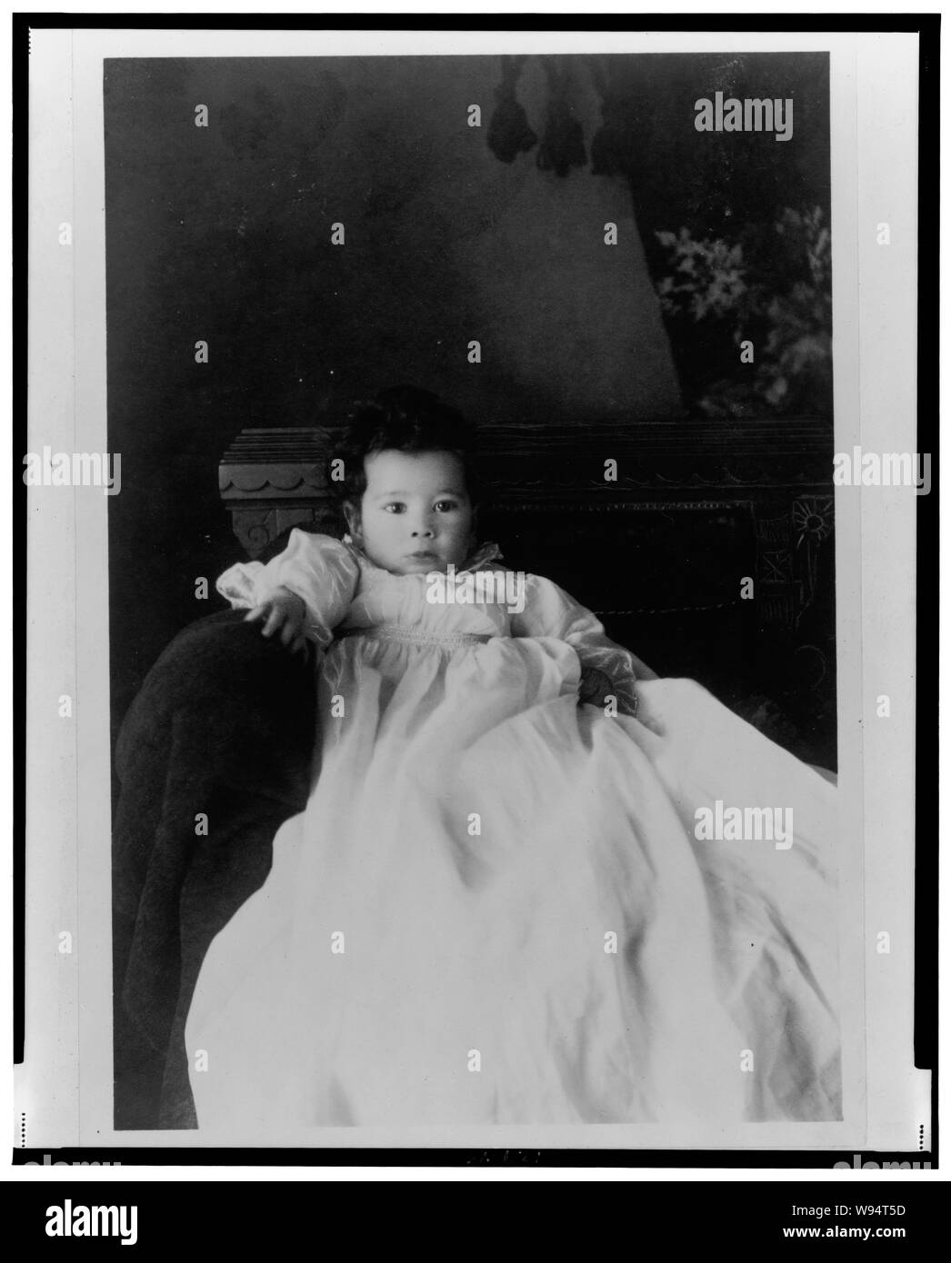 African American infantile, seduto nella sedia, indossare un abito battesimo, rivolto verso la parte anteriore Foto Stock