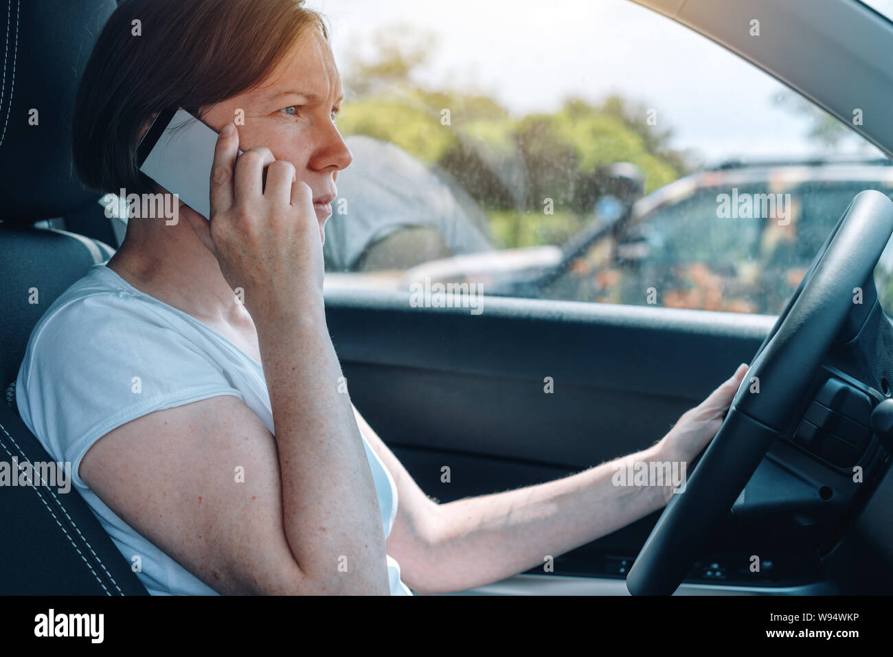 Donna alla guida di auto off-road e parlando al telefono cellulare, vista laterale da un sedile del passeggero di adulto femmina caucasica persona con smartphone la presa Foto Stock
