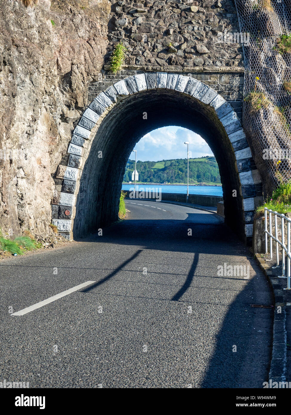 Nero tunnel ad arco con cadute di massi, frane protezione netto e Causeway percorso costiero. Scenic coast road nella contea di Antrim, Irlanda del Nord Foto Stock