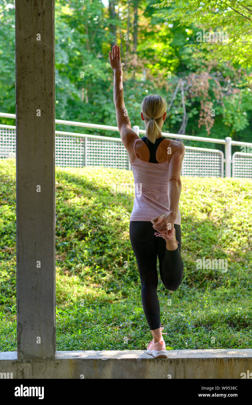 Athletic donna facendo il riscaldamento esercizi di allungamento i suoi muscoli delle gambe prima di un allenamento e un braccio in alto Foto Stock