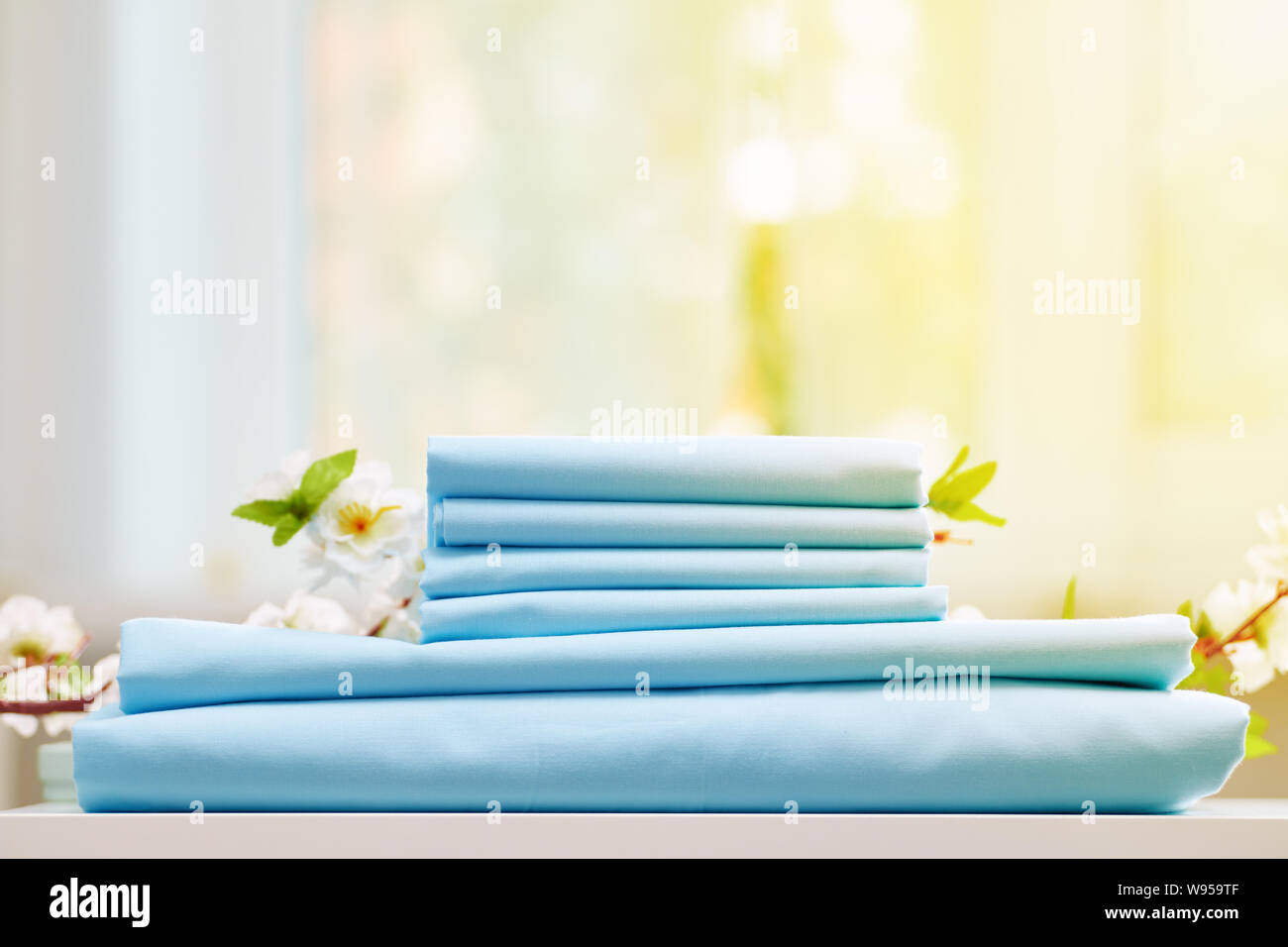 Una pila di blu biancheria da letto ripiegato su una scrivania. Ramo di fioritura. Sfondo sfocato. Foto Stock
