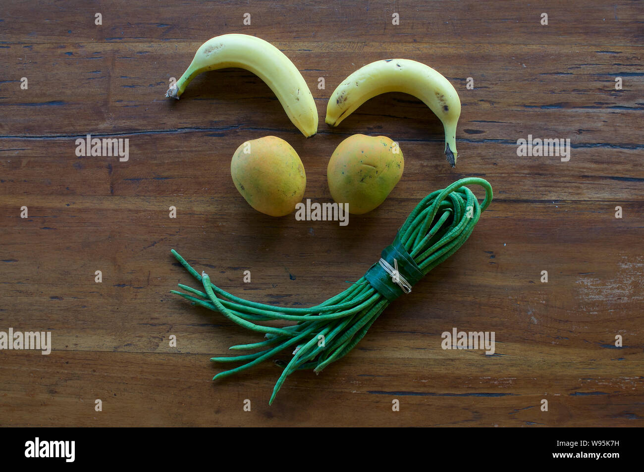 Un divertente grimace realizzata in diversi tipi di frutta e verdura su una tavola di legno Foto Stock