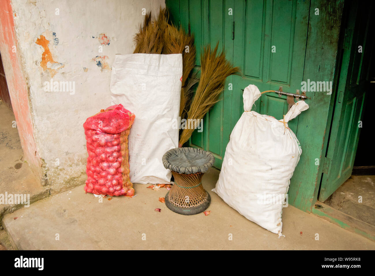Erba di scope e sacchi di cipolle e grano appoggiarsi contro un edificio in vecchio bazaar area di Pokhara, Nepal Foto Stock
