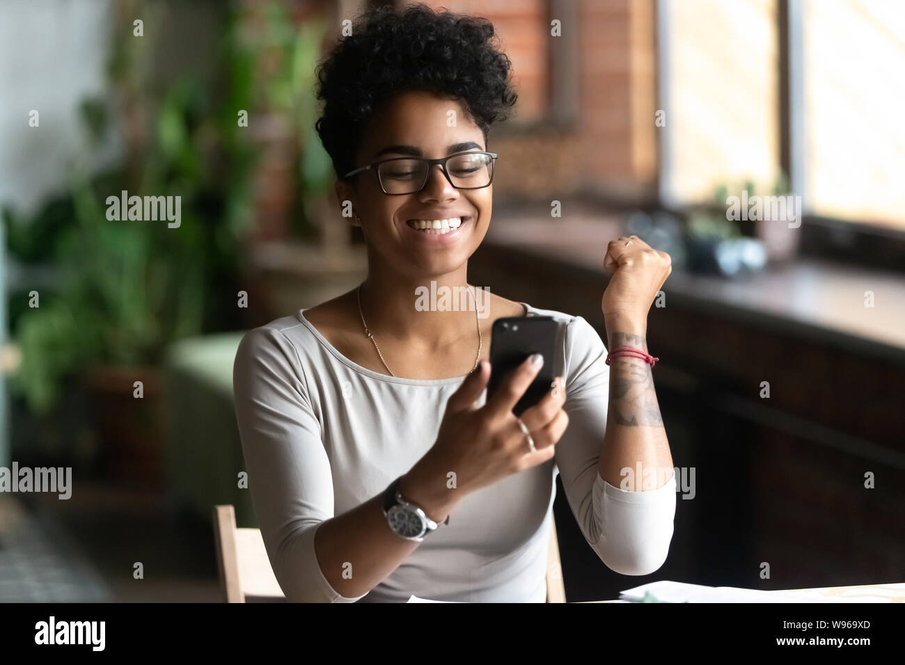 Eccitato nero ragazza sente euforici per leggere le notizie sul cellulare Foto Stock