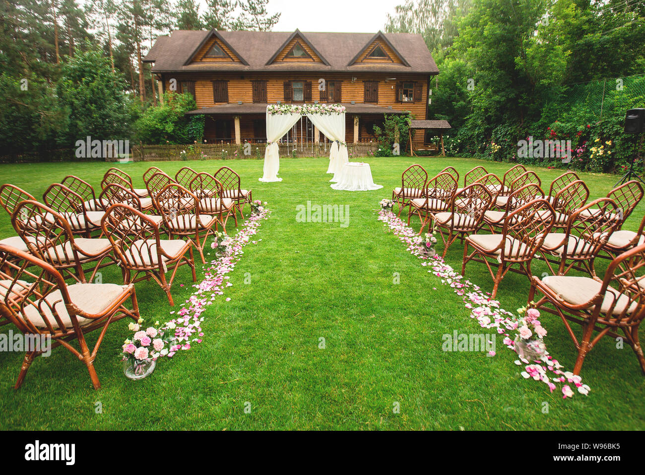 Outdoor cerimonia nuziale decorazione setup. Percorso con petali, sedie decorate con nastri colorati, bianco arch. concetto di matrimonio Foto Stock