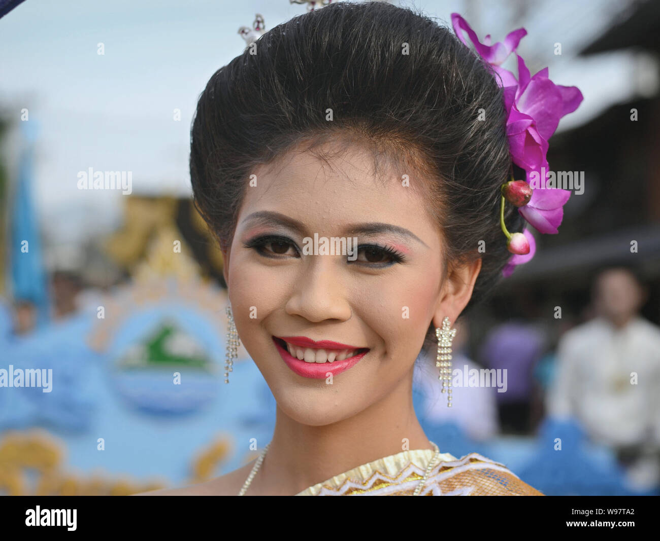 Vestite tailandese graziosa ragazza con i fiori nei capelli prende parte del villaggio Lanna storico street parade e sorrisi per la fotocamera. Foto Stock