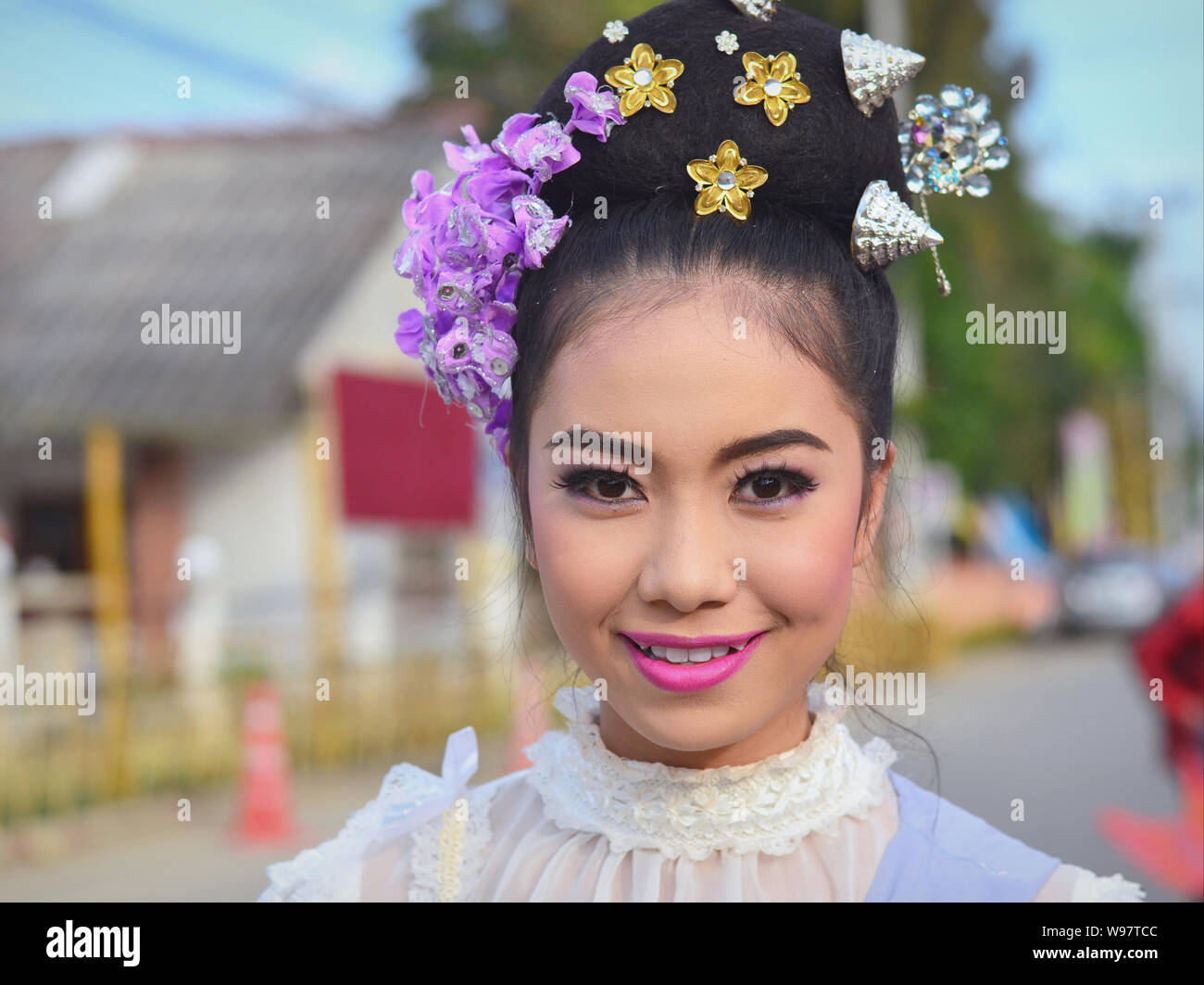Vestite bella ragazza Thailandese con fiori nei capelli prende parte del villaggio Lanna storico street parade e sorrisi per la fotocamera. Foto Stock